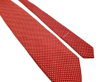 May include: A red tie with a repeating pattern of small, light-colored shapes. The tie is made of a smooth fabric and features the brand name "GIORGIO ARMANI" on a label near the tip. The tie is a classic accessory.