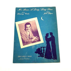 May include: Vintage sheet music titled "It's Been A Long, Long Time" with lyrics by Sammy Cahn and music by Jule Styne. The cover features a portrait of a man, a silhouette of a couple, and a crescent moon on a blue background.
