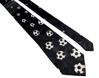 May include: Black necktie with a repeating pattern of white soccer balls. The tie has a textured, patterned background. The tie is angled across a white background.