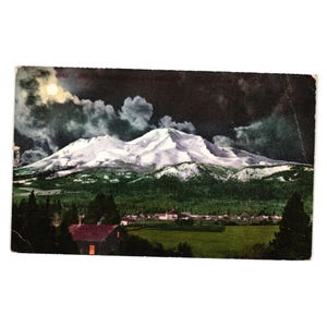 Könnte beinhalten: Vintage Postkarte mit einer nächtlichen Landschaft eines schneebedeckten Berges unter einem bewölkten Himmel mit Vollmond. Eine kleine Stadt und grüne Felder befinden sich im Vordergrund. Die Postkarte ist leicht gealtert.