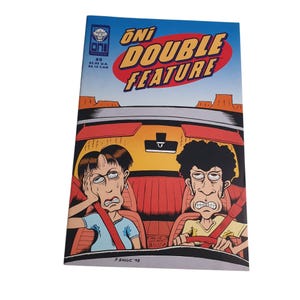 May include: Comic book cover for Oni Double Feature #9. The cover features a cartoon illustration of two people in a car, with the title in a red and yellow banner. The background shows a desert landscape. The comic is dated 1998.