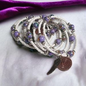 May include: A multi-strand bracelet made of white and lavender beads with a silver charm featuring a wing and a spiral design.