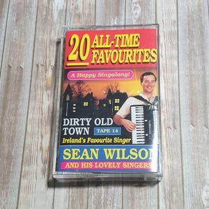 May include: A vintage cassette tape titled "20 All-Time Favourites" featuring "Dirty Old Town" by Sean Wilson and his Lovely Singers. The cover has a red and yellow design with a photo of the singer playing an accordion.