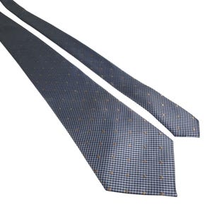 May include: A blue and white patterned tie with small brown dots. The tie is made of a woven fabric and is angled across a white background. The tie is a classic accessory for formal or business attire.