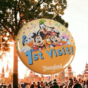 Op de afbeelding: Een grote, ronde Disneyland Resort-knop met de tekst "1st Visit!" in blauw. De knop toont Mickey Mouse, Minnie Mouse, Donald Duck, Daisy Duck en Goofy. De achtergrond is lichtgeel met confetti.