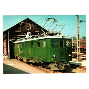 May include: Vintage postcard featuring a green electric train, marked with "SBB CFF" and number 909. The train is parked in a station, with a wooden structure in the background. The sky is a clear blue.
