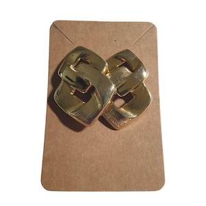 May include: Gold-toned, geometric earrings with a linked design. The earrings are square-shaped with a textured surface, and are displayed on a brown card.