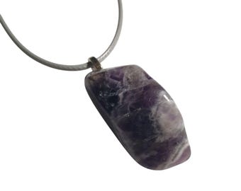 May include: A polished amethyst pendant with a silver-tone bail, suspended from a gray cord. The gemstone displays a mix of purple and white hues. The pendant is a rectangular shape with rounded edges.