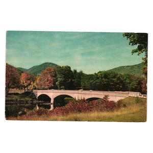 May include: A vintage postcard featuring a scenic view of a concrete bridge over a river. The bridge has three arches and is surrounded by lush green trees and hills. The sky is a light blue with a few clouds. The postcard is in good condition with some minor wear and tear.