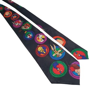 May include: A black silk tie with a repeating pattern of colourful circles featuring cartoon characters from the Looney Tunes franchise. The characters include Tweety Bird, Wile E. Coyote, Road Runner, Bugs Bunny, and Sylvester the Cat.