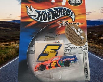 Op de afbeelding: Een Hot Wheels Racing 2002 die-cast auto van Terry Labontes #5 Kellogg's Frosted Flakes NASCAR raceauto. De auto is oranje, zwart en blauw met een sticker van de auto op de achterkant van de verpakking.