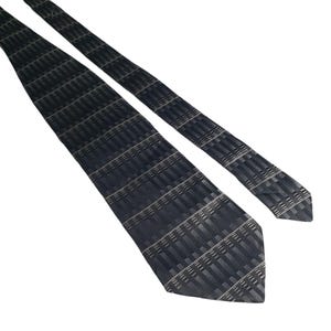 May include: A dark blue tie with a repeating geometric pattern of rectangles and lines in shades of gray and white. The tie is angled across a white background.