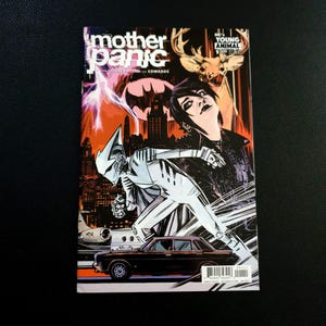 May include: A comic book cover for "Mother Panic" features a stylized illustration. The cover art includes a figure in a white and silver suit, a black car, and a woman with dark hair. The title is in white and pink, with a cityscape and lightning in the background.