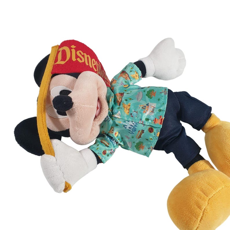 May include: A plush Mickey Mouse toy wearing a blue and green shirt with a Disney park print, black pants, and a red hat with the word "Disney" on it.