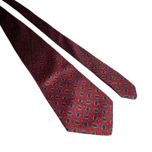 May include: A red necktie featuring a repeating pattern of small, oval-shaped motifs in shades of blue, yellow, and black. The tie has a pointed end and a smooth, woven texture, displaying a consistent geometric design across the entire fabric surface.
