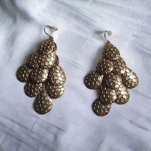 May include: A pair of gold-tone dangle earrings with a cascading design of textured, round, and teardrop-shaped metal pieces.