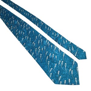 May include: A blue necktie with a repeating white sperm cell pattern. The tie is angled across a white background. The tie's design features a speckled texture.