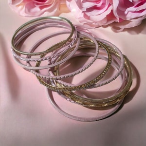 May include: A set of pink and gold bangles. The bangles are stacked on top of each other and have a shiny finish.