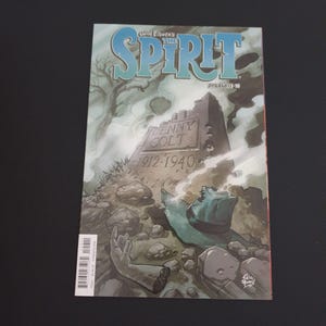 May include: Comic book cover for Will Eisner's The Spirit, Dynamite #10. The cover art features a tombstone with the name Denny Colt and the years 1912-1940. The background includes a tree, a hand, and a hat.