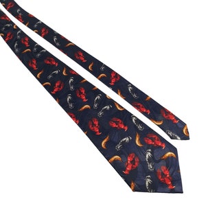 以下が含まれることがあります： 赤いロブスターと金色と銀色の魚が繰り返し描かれた、濃い青色のシルクネクタイです。