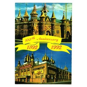 Puede incluir: Una postal vintage que presenta el Mitchell Corn Palace, celebrando su 100 aniversario de 1892 a 1992. La imagen muestra la arquitectura única del edificio con agujas y cúpulas ornamentadas, sobre un cielo azul.