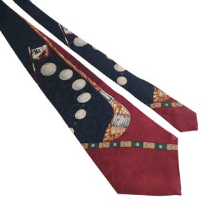 Può includere: Una cravatta di seta rossa e blu navy con un motivo di mazza da golf e palline da golf. La cravatta ha uno sfondo rosso con una striscia blu navy e una mazza da golf dorata con una pallina da golf bianca all'estremità. La cravatta è decorata con palline da golf bianche e una bandiera da golf verde e bianca.