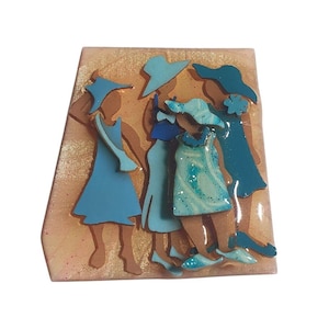 Puede incluir: Una placa decorativa de pared con un diseño tridimensional en capas de cuatro figuras que llevan sombreros y vestidos en varios tonos de azul. Las figuras están sobre un fondo de color tostado claro y texturizado con un acabado brillante.
