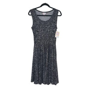 May include: Sleeveless black and white speckled dress hanging on a black hanger. The dress has a scoop neckline and a flared skirt. A tag is attached to the dress.
