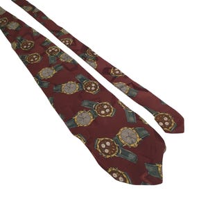 May include: A maroon necktie featuring a repeating pattern of gold and silver wristwatches with green watchbands. The tie is made of a smooth fabric and is angled across a white background.
