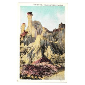 May include: Vintage postcard featuring a colorful landscape of rock formations in Wyoming. The image shows a towering rock structure with a reddish-brown top, set against a light blue sky. The text "THE SENTINEL. HELL'S HALF ACRE, WYOMING" is printed at the top.