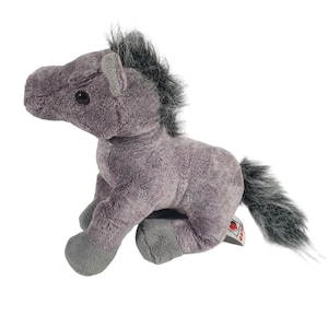 Op de afbeelding: Een grijs pluche paard met een donkergrijze manen en staart. Het knuffel heeft een getextureerde body en kleine zwarte ogen. Het paard zit met zijn benen onder zich.