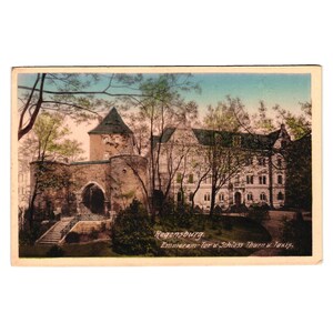 Op de afbeelding: Een vintage ansichtkaart met een ingekleurde illustratie van de Emmeram-Tor en Schloss Thurn und Taxis in Regensburg. De scène toont een stenen poortgebouw met een toren en een groot gebouw omringd door bomen, met de tekst Regensburg Emmeram-Tor u Schloss Thurn u. Taxis in de rechterbenedenhoek.