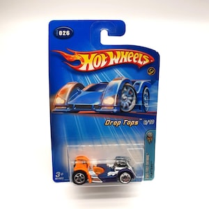 May include: A Hot Wheels die-cast toy car in its original packaging. The car is a Drop Tops model, with a blue body, orange accents, and silver wheels. The packaging is blue with the Hot Wheels logo and the text "Drop Tops 6/10".