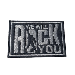May include: A rectangular black patch with white embroidered text that reads "WE WILL ROCK YOU". The patch features a silhouette of a person playing a guitar. The border is white.