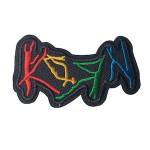 May include: Embroidered patch with the word "KAYN" in colorful thread. The letters are red, yellow, green, and blue, stitched onto a black fabric background. The patch has a wavy, irregular shape.