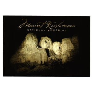 May include: A dark image featuring Mount Rushmore National Memorial. The monument of four U.S. presidents is illuminated against a black background. The text "Mount Rushmore NATIONAL MEMORIAL" is written in a cursive font.