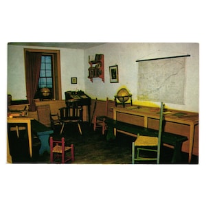 May include: Vintage postcard image of a classroom interior. The room features wooden desks, chairs, and a map on the wall. A globe sits on a desk near a window with a red curtain. The room is lit by natural light.