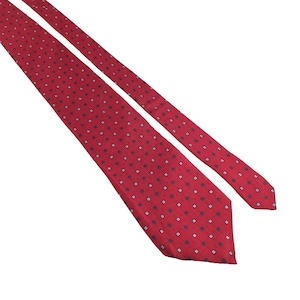 Puede incluir: Una corbata roja con un patrón repetitivo de pequeños cuadrados azul oscuro y blancos. La corbata está en ángulo sobre un fondo blanco, mostrando su textura y diseño. La tela de la corbata parece ser un material tejido.