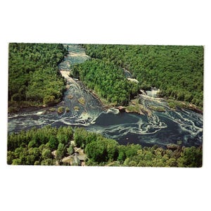 Puede incluir: Postal vintage con una vista aérea de un río que serpentea a través de un exuberante bosque verde. El agua es oscura con áreas blancas y espumosas, y un pequeño edificio es visible cerca de la orilla.