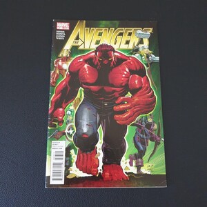 May include: A comic book cover for "The Avengers" featuring a large, red-skinned character in jeans. The title "The Avengers" is in large, yellow letters. Other characters are visible in the background. The comic is on a black surface.
