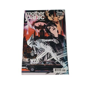May include: A comic book titled "Mother Panic" with a vibrant cover featuring a stylized illustration. The artwork includes a figure in a white and silver suit, a black car, and a cityscape backdrop with lightning and a bat symbol.