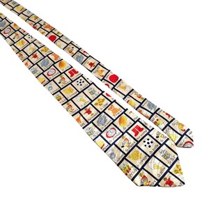 以下が含まれることがあります： フランス語の単語と日常的な物のイラストが描かれた青い正方形が繰り返されるパターンが施された、ベージュのシルクネクタイ。ネクタイは赤と白の縁取りが施されています。