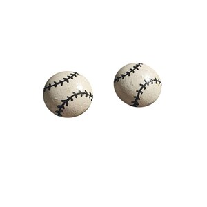 May include: Two baseball-themed earrings. Each earring is a small, round, off-white ball with black stitching details, resembling a baseball. The earrings are set against a plain white background.