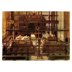 May include: A postcard image of a cathedral interior featuring two ornate, carved stone tombs. The tombs are enclosed by wrought iron railings and are positioned in front of a large, intricately carved wooden screen. The overall color palette is warm, with shades of brown and gold.