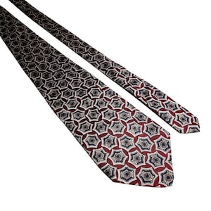 May include: A burgundy tie with a repeating pattern of navy blue and beige star-like shapes. The tie is made of a smooth fabric and is angled across a white background.