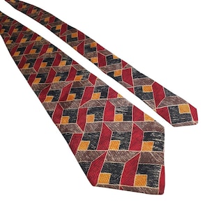 Peut inclure: Une cravate présentant un motif géométrique répétitif de cubes imbriqués dans des tons de rouge, noir, marron et jaune. Le tissu présente une finition texturée visible sur tout le motif, avec une extrémité pointue et une forme effilée.