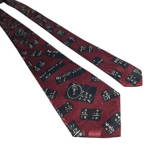 May include: A burgundy tie with a repeating pattern of black rectangles containing mathematical equations and symbols. The tie is made of a shiny material and is angled across a white background.