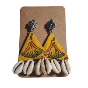 May include: A pair of handmade earrings featuring yellow fabric triangles with a floral pattern in orange, green, and red. The earrings are adorned with white cowrie shells and silver-colored floral studs.