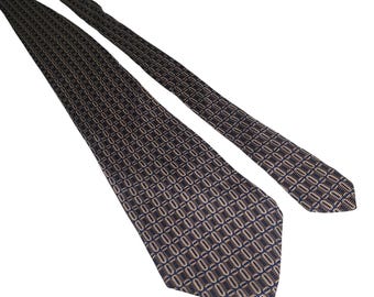 May include: A patterned necktie in shades of navy blue, brown, and beige. The tie features a repeating geometric design. The tie is angled across a white background, showcasing its length and pattern.