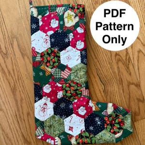 Może przedstawiać: Pikowana pończocha świąteczna z patchworkowym wzorem. Pończocha ma różne świąteczne wzory, w tym Świętego Mikołaja, bałwanki i jagody ostrokrzewu. Tekst "PDF Pattern Only" znajduje się w białym okręgu.